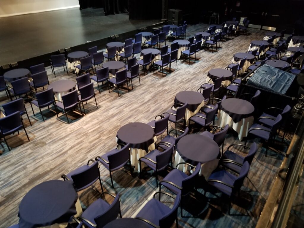 blue chairs cabaret style around round tables in a theatre